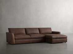 a brown leather sectional sofa sitting on top of a cement floor next to a white wall