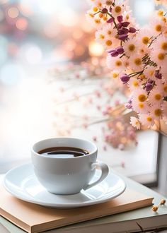 a cup of coffee sitting on top of a book next to a vase with flowers