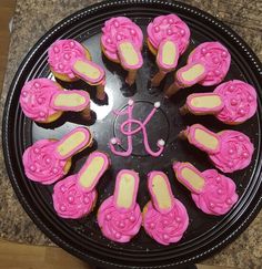 cupcakes decorated with pink icing are arranged in a circle on a black platter