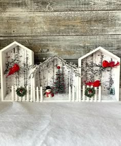 three white houses decorated with red birds and christmas decorations on snow covered ground next to wooden planks