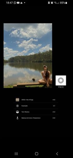 a woman sitting on a bench next to a body of water with clouds in the background