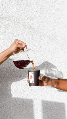 a person pouring wine into a cup on top of a white table with a black coffee mug