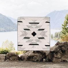 a large white and black quilt sitting on top of a pile of rocks next to a lake