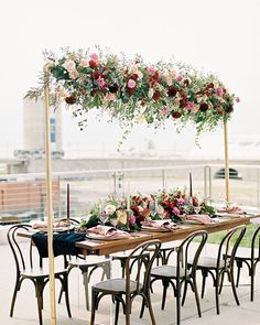 an outdoor dining table set up with flowers and greenery on it for a wedding reception