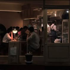 people are standing in the window of a restaurant at night, and one person is preparing food