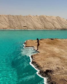 a person standing on the edge of a cliff overlooking water and sand hills in the background