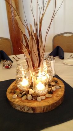 some candles are sitting in mason jars on a wooden stand with rocks and branches around it