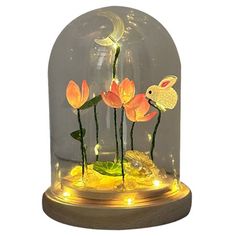 a glass dome with some flowers in it and a bunny on the side, under a light up base