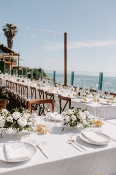 an outdoor dining area with white table cloths and place settings set for dinner by the ocean