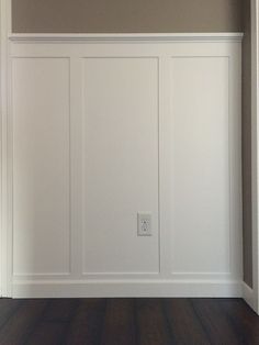 an empty room with white paneling and wood floors