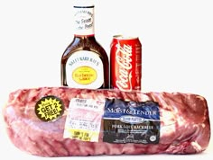 a large piece of meat sitting next to two cans of soda