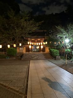 a walkway with steps leading up to a building and lanterns hanging from the roof at night