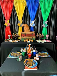 a table topped with plates covered in colorful paper curtain decorations and decorating items on top of black tables cloths