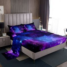 a bed room with a neatly made bed covered in purple and blue galaxy comforters