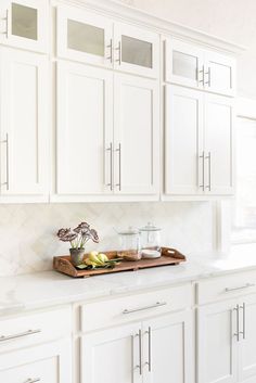 a kitchen with white cabinets and wooden cutting board on the counter top in front of it