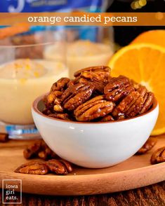 a bowl filled with orange candied pecans sitting on top of a wooden table