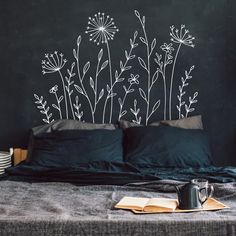 a black wall with white flowers painted on it next to a bed and some plates