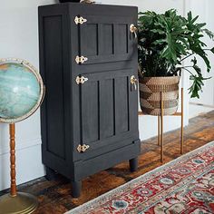 a black cabinet sitting on top of a wooden floor next to a potted plant