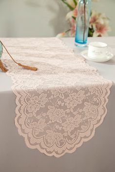 a lace table runner on top of a white table with blue vases and flowers in the background