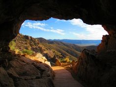 a view from inside a cave looking out at mountains and valleys in the distance with blue skies above