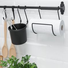 a pot and two wooden spoons hanging on a wall next to a toilet paper holder