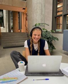 a woman sitting at a table with a laptop computer in front of her, smiling