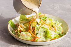 a person pouring dressing onto a salad in a bowl