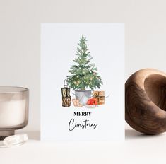 a card with a christmas tree on it next to a glass of water and a wooden object