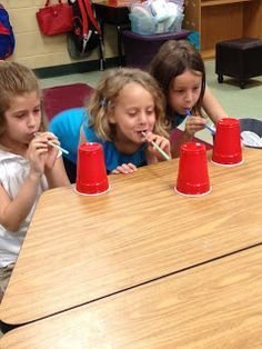 three young children sitting at a table with red cups on it and one child brushing their teeth