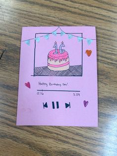 a pink card with a birthday cake on it sitting on top of a wooden table