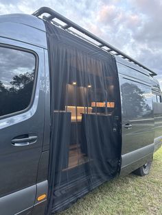 a van with its door open and curtains pulled up to the side, sitting on grass