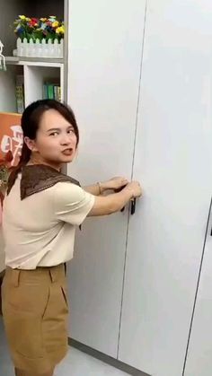 a woman standing in front of a white cabinet holding onto the handle on a door