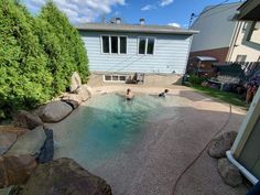 two people playing in an outdoor pool surrounded by rocks and grass with houses in the background