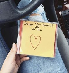 someone holding up a cd with a heart drawn on it in the back seat of a car