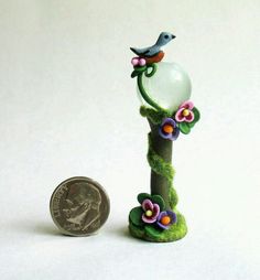 a tiny bird perched on top of a green pole next to a coin and white background