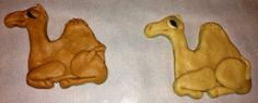 two clay camels sitting next to each other on a white counter top, one is yellow and the other is brown