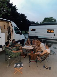 a group of people sitting around a table in front of a camper van with the door open