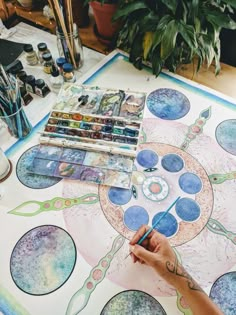 a person is painting on a table with paintbrushes and watercolors in front of them