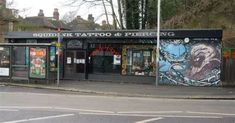 an outdoor tattoo parlor on the corner of a street with trees and buildings in the background