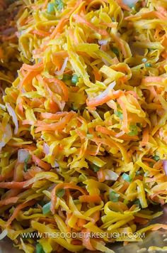 shredded carrots and other vegetables are mixed together in a large metal bowl on the table