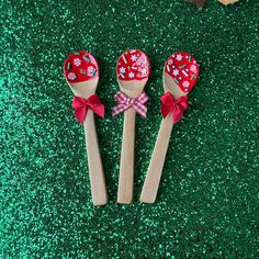 three wooden spoons decorated with red flowers and bows on green glittered ground next to cookies