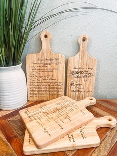 two wooden cutting boards sitting on top of a table next to a potted plant