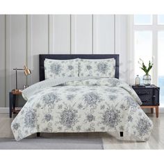 a bed with white and blue flowers on it in a room next to a window