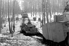 two tanks driving down a snowy road next to trees and people on top of them