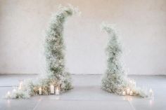 two tall white pillars with candles in front of them and some bushes on the ground