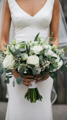 a bride holding a bouquet of white flowers and greenery