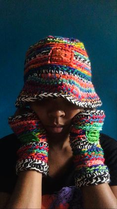 a woman wearing a multicolored crocheted hat and arm warmers with her hands on her face