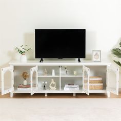 a flat screen tv sitting on top of a white entertainment center next to a potted plant