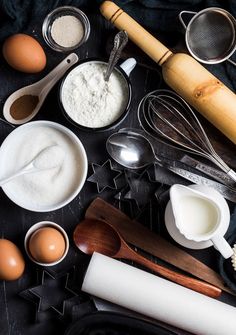 an assortment of baking ingredients on a black table with utensils and spoons