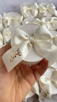 a hand holding a small white box with a bow on the front and monogrammed initials on the side